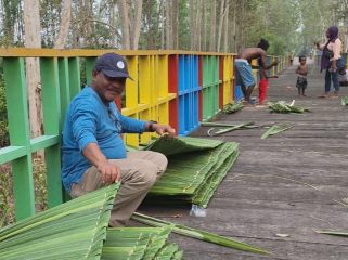 Petrus Kasihiw tengah menganyam daun sagu untuk dijadikan atap pondok di kampung Masina, Bintuni.